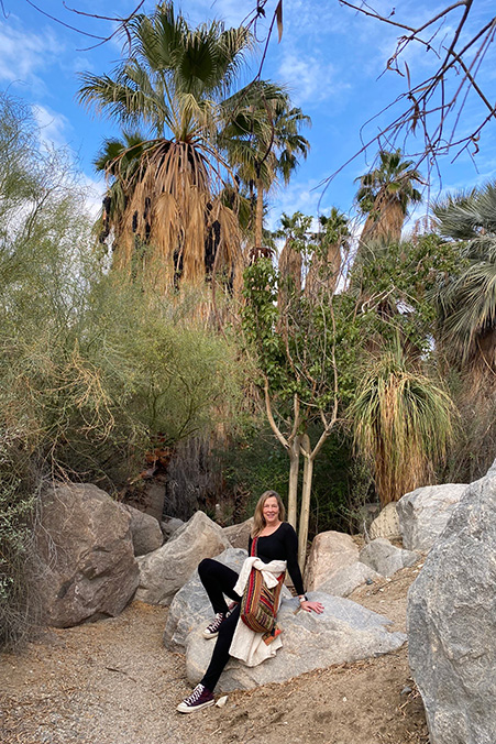 Barbara Payne sits on a rock in front of palm trees