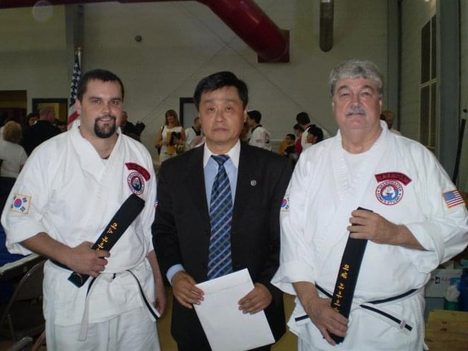 Russ Carmichael in a martial arts uniform standing with two other men