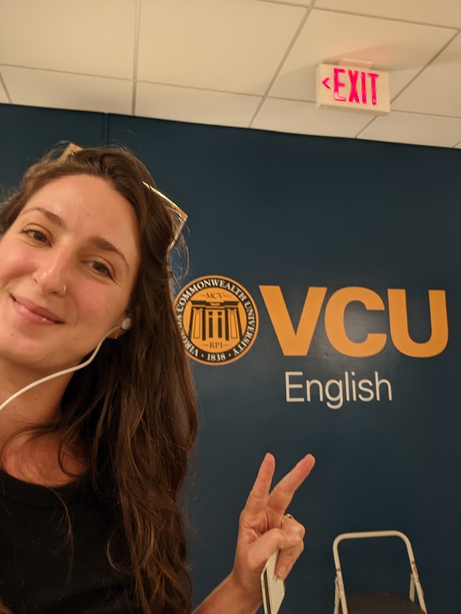 Kelsey Cappiello poses in front of a VCU English logo painted on a wall